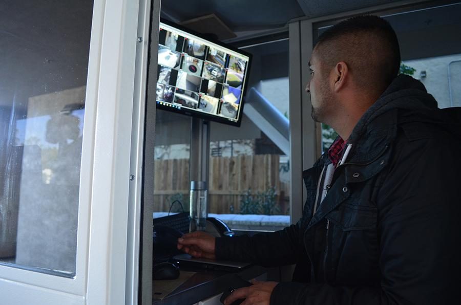 WATCHFUL: Manny Fernandez, Director of Security, monitoring cameras from the gate-control booth in the driveway.  Below, the front gate of the school extends to driveway roof and cannot be climbed.