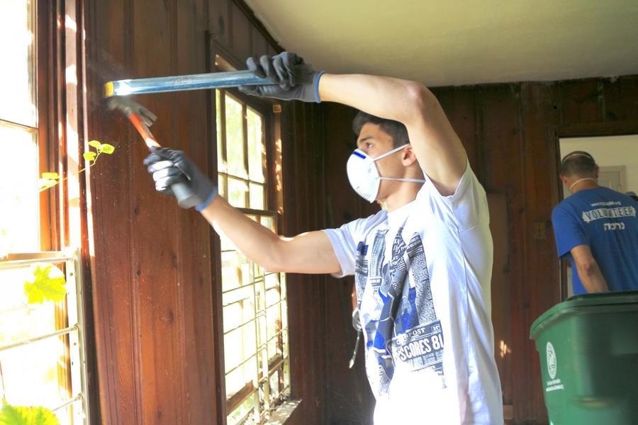 Zack Muller uses a crowbar and a hammer to remove a window frame from the wall.