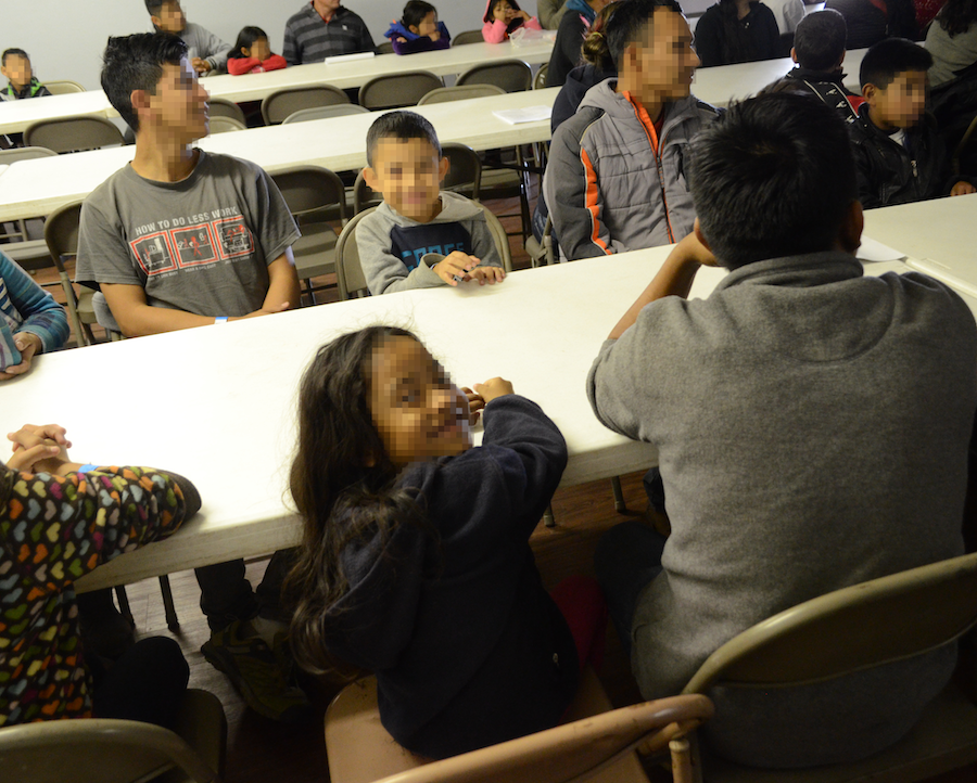 Two children smile as Pastor Ramon Madrid welcomes the migrant families and explains the process of sending them out to their host families across the United States. 