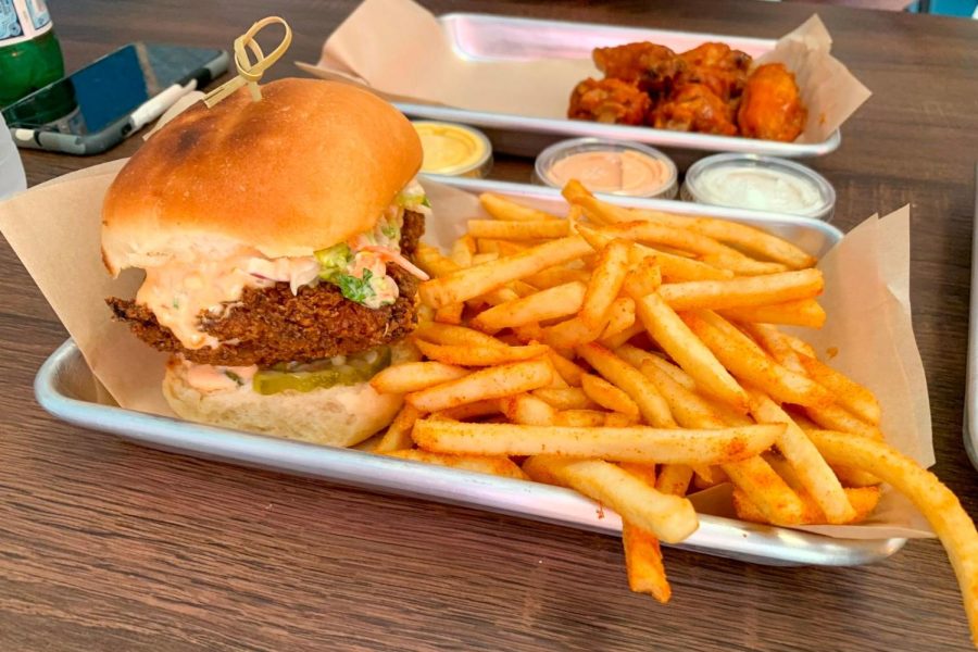 Food from Melrose Bite; burger with fries in forefront, mango habanero chicken wings and sauces in background