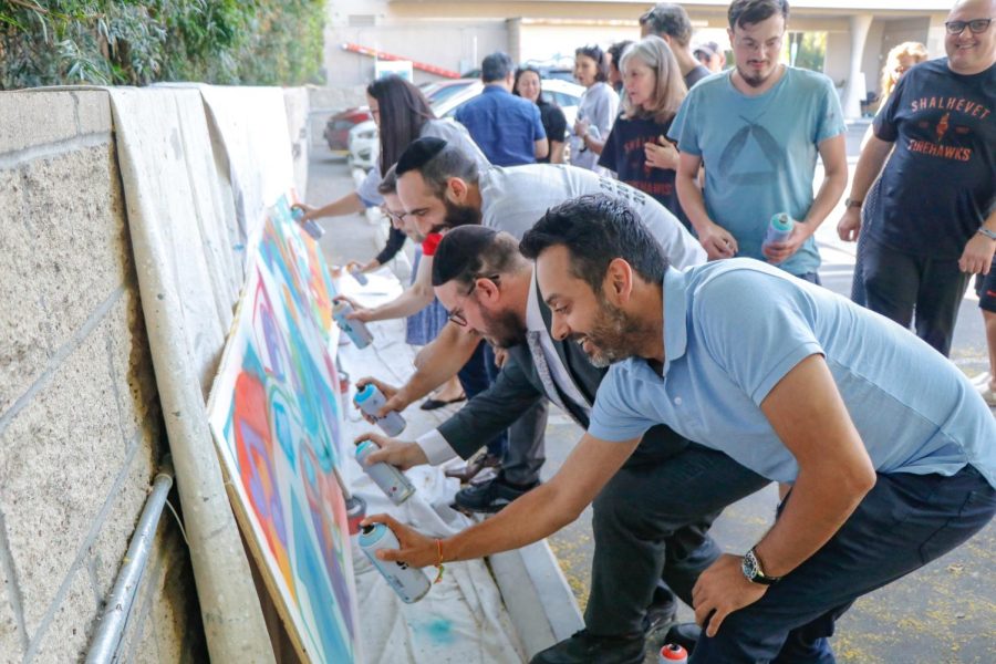 GROUP: Mr. Souza, standing in light blue shirt, supervises as faculty and staff spray paint a mural he designed during back-to-school meetings last August.