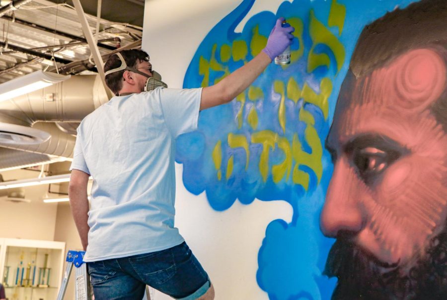 DETAIL: Souza works on cafeteria spray painting Theodore Herzl and his famous quote. The painting of Herzl is darkly colored, but the words and background around him contrast with bright paint.