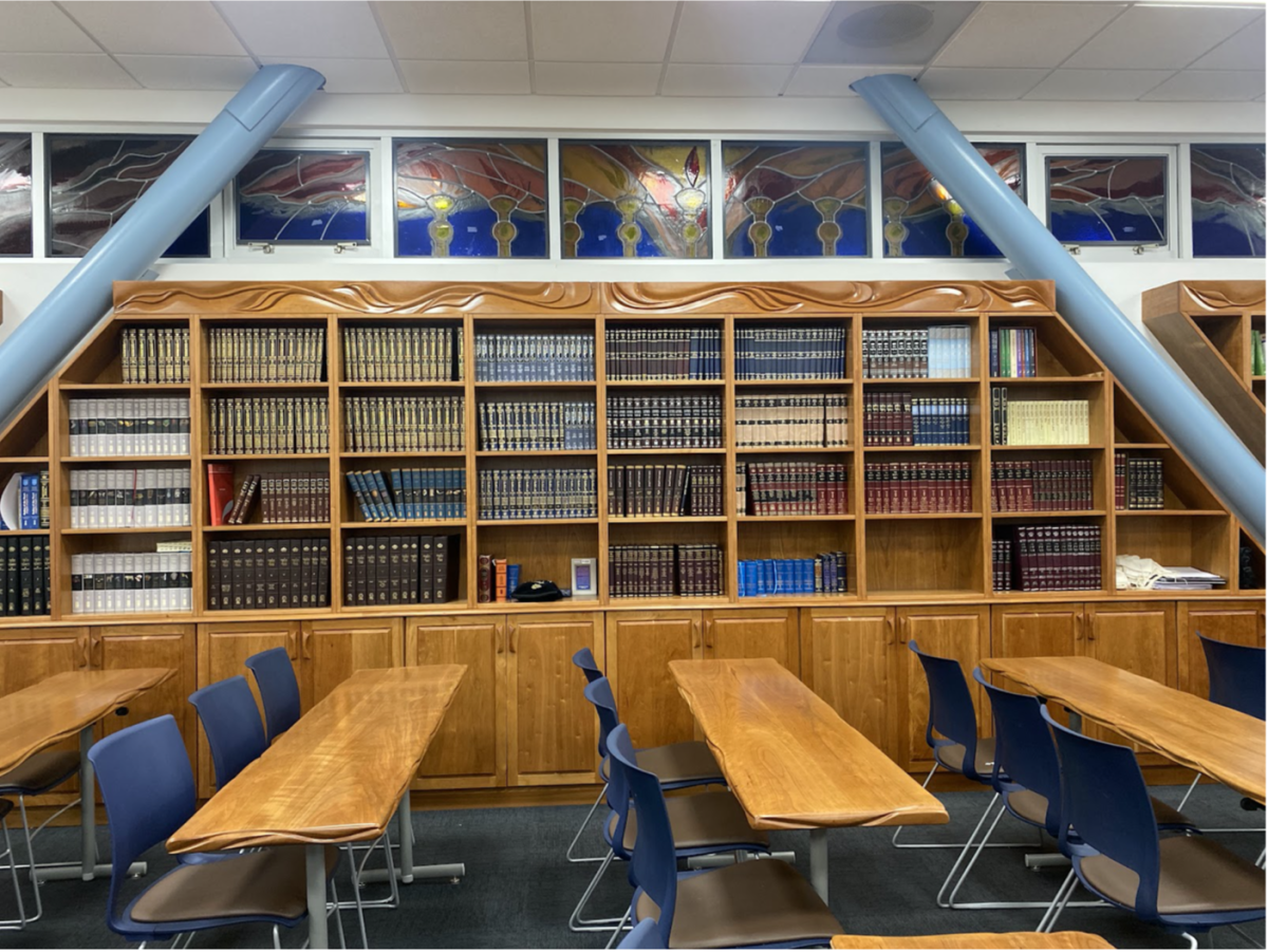 Viewed from the north-facing wall, sets of Shas, Mishneh Torah and commentaries on Tanach are among the many religious books purchased to fill the Beit Midrash shelves. Above them are horizontal stained-glass windows with representations of Shabbat and holidays. 
