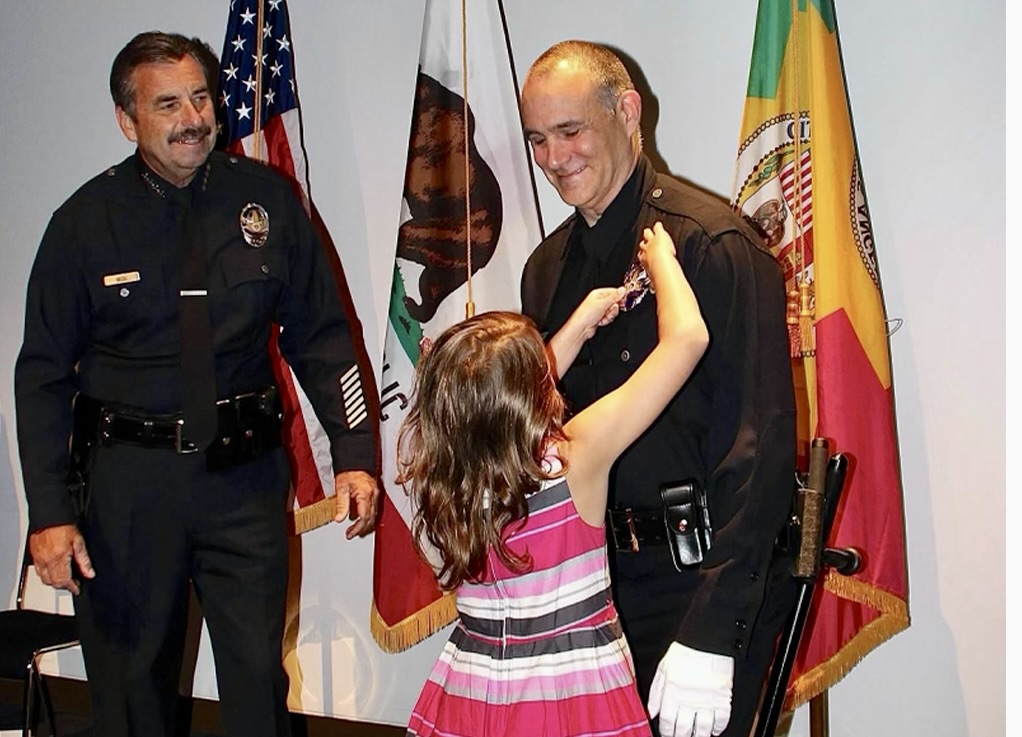 SERVICE: Ivan Wolkind zl smiles as his daughter Nettie, now a Shalhevet senior, affixes his badge at his LAPD swearing-in ceremony July 2, 2014, as then-Chief Charlie Beck looks on. Mr. Wolkind was known in the Jewish community and beyond as a champion of safety and love of family. 