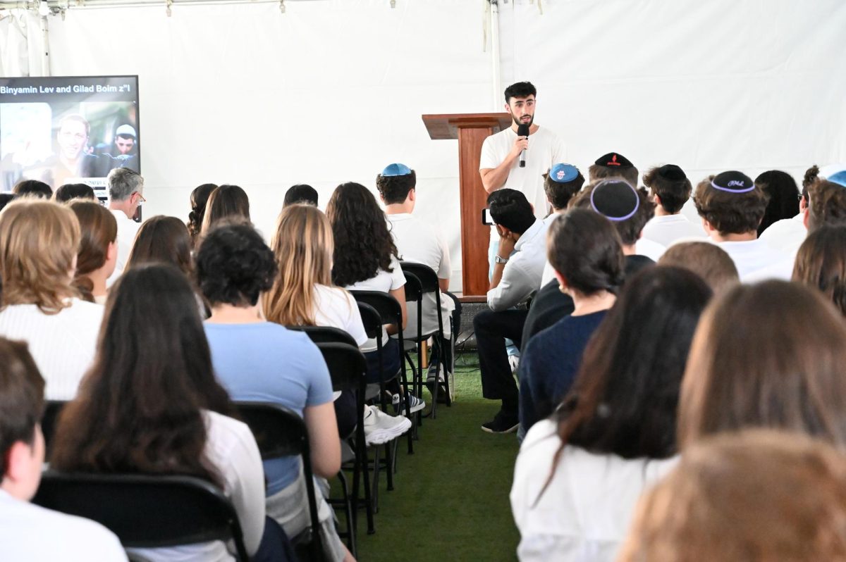 SOLDIER: Alumnus Mitchell Hoenig ‘20 speaks to students and teachers about his experience on Oct. 7 in Israel, serving in IDF reserves afterwards, and about his two friends – one who died fighting on Oct. 7, and one who was killed in Gaza months later. To start off the assembly on the roof, students and teachers clad in blue and white watched a video of the destroyed homes and buildings on kibbutzim in southern Israel after the Oct. 7 Hamas attacks 