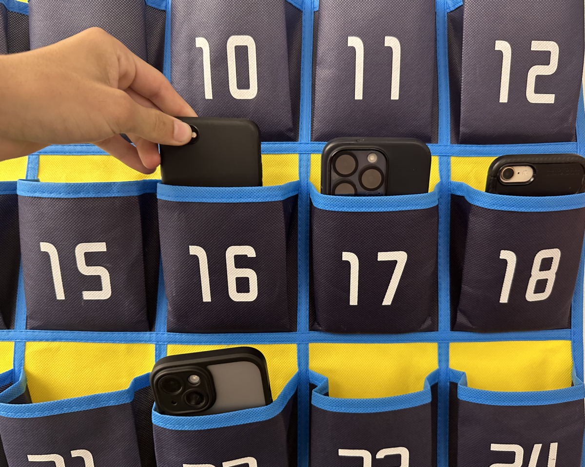 POCKET: Junior Zachary Schechter places his phone in a wall-hanging cell phone holder before his English class begins. A first, second and third offense system is used for consequences if a student is caught with their phone.


