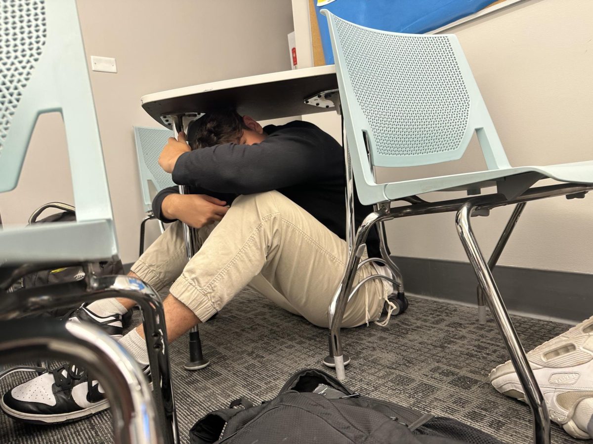 DUCK: Senior Ariel Caruthers takes cover under a desk in Dr. Sheila Keiter’s World War II class. When the drill announcement went out over the loudspeakers, every student in the class hunched beneath their desks. 